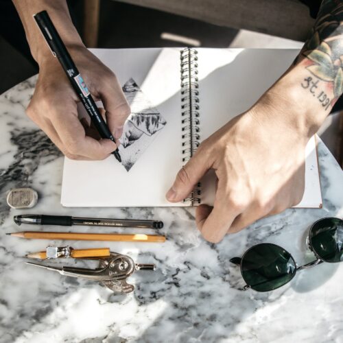 Praktykant studia tatuażu tworzący szkic tatuażu na stronie zeszytu, rozwijając swoje umiejętności rysowania.