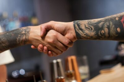 Uścisk dłoni pomiędzy praktykantem studia tatuażu a doświadczonym tatuatorem, symbolizujący współpracę i naukę w branży.